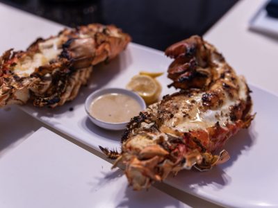 Grilled lobster tail with a side of butter sauce and lemon wedge.